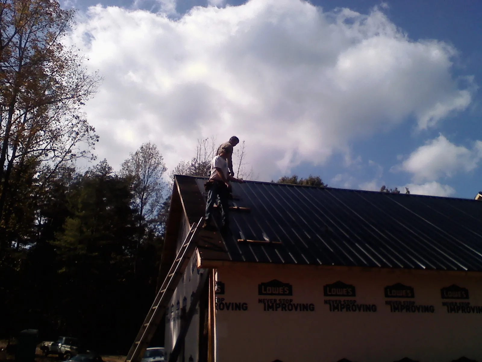 Roofer fastening dark metal panels high against a cloudy sky, from a Roof Inspection job in Oxford