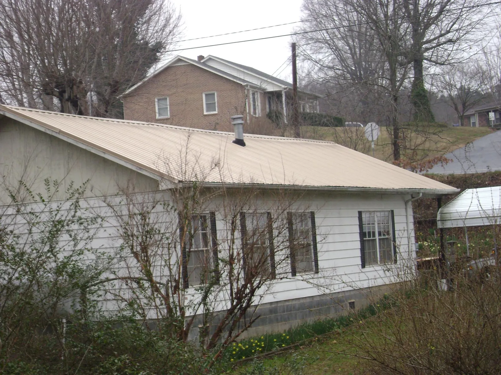 Tan metal roof on a white sided house set into a hillside — Commercial Roofing by Roofing Brothers in Oxford